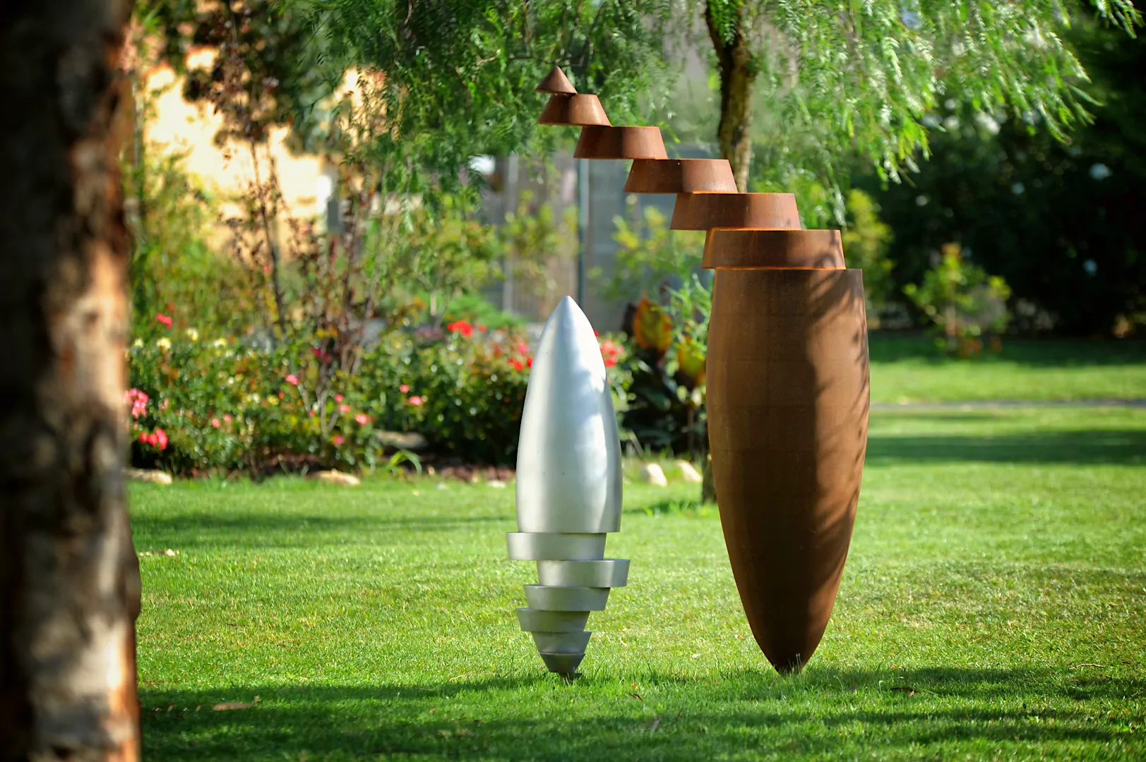 Ensemble d'art contemporain composé de 2 sculptures en métal (inox 316L et acier corten) exposées dans un jardin. Oeuvre de Félix Valdelièvre, sculpteur métal.