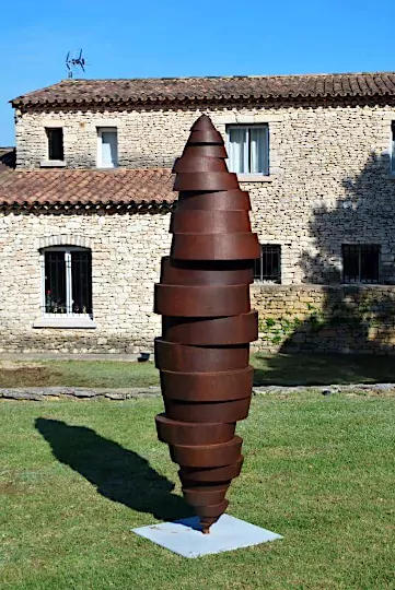Photographie de la sculpture monumentale Vibration, exposée en extérieur, devant une maison provençale - Oeuvre du sculpteur sur métal Félix Valdelièvre
